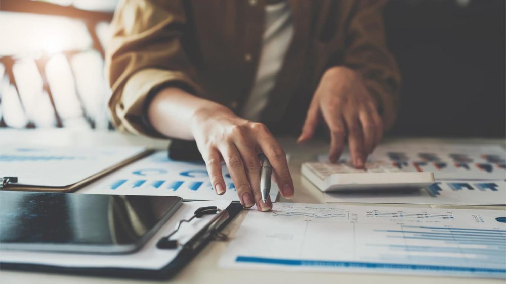 Close up of business woman or accountant working on calculator to calculate business data, accountancy document and laptop computer at office, business concept