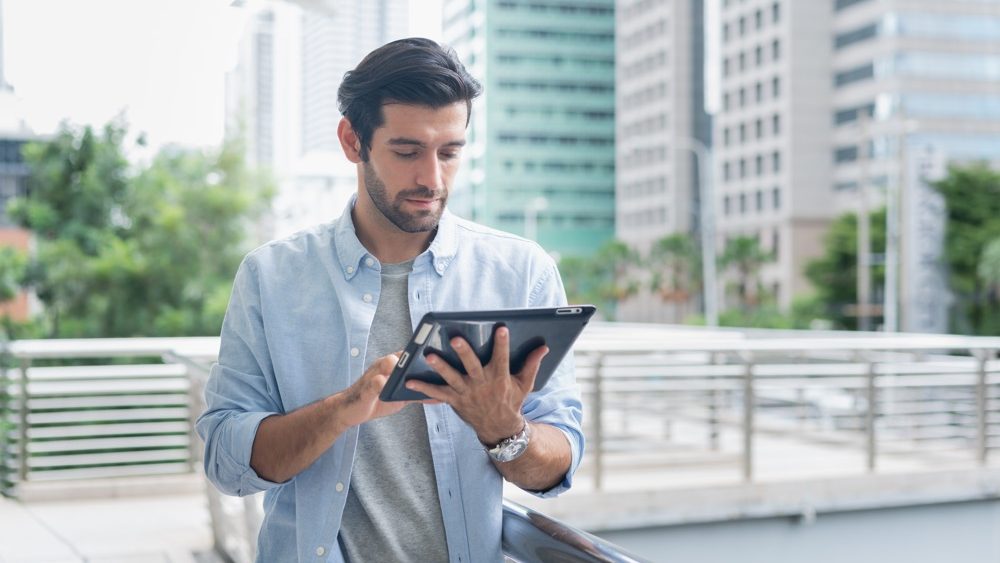 Young man using laptop computer working and video conference meeting at outdoor. Young creative man looking at screen typing message with tablet.Handsome young man using digital tablet